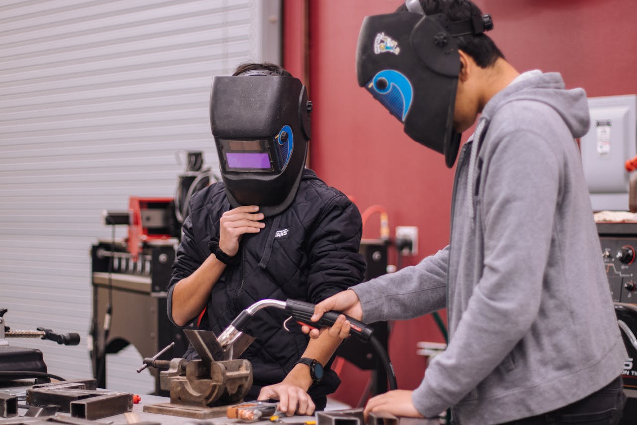 Services-02 Two welders in protective gear concentrate on a project in a workshop setting.