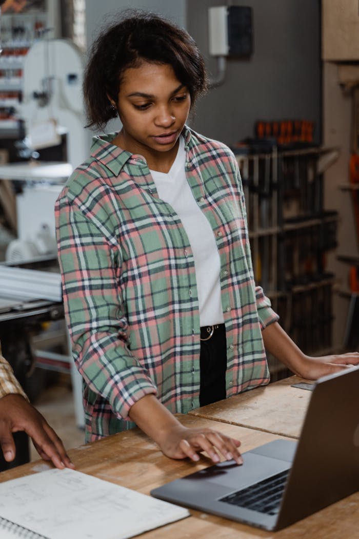 Crafting Captivating Headlines: Your awesome post title goes here A young woman in a workshop using a laptop to manage woodworking tasks.